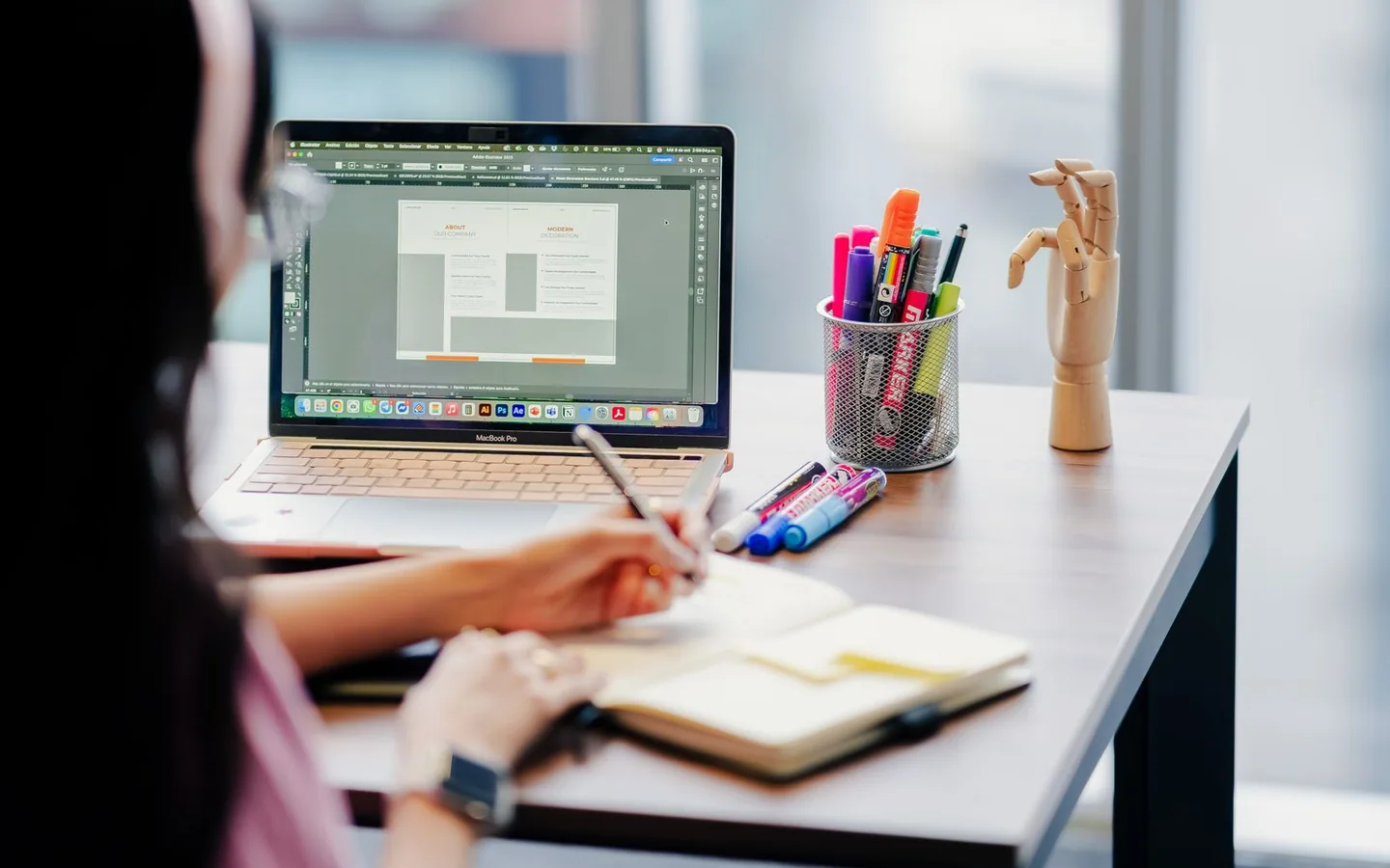 A designer sketching ideas beside a laptop in a modern workspace