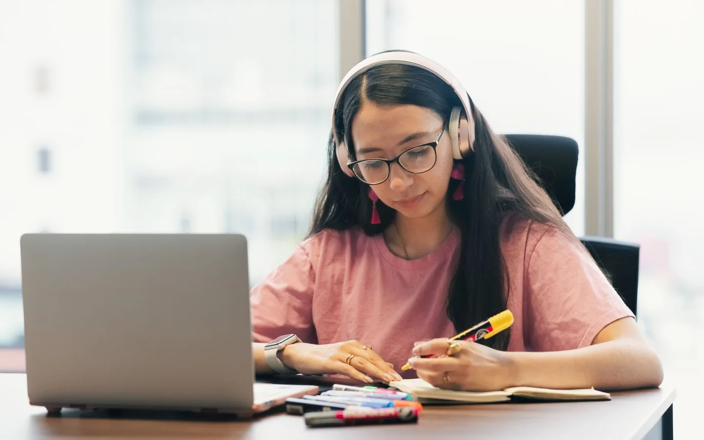 A person learning with headphones, a laptop and a notebook